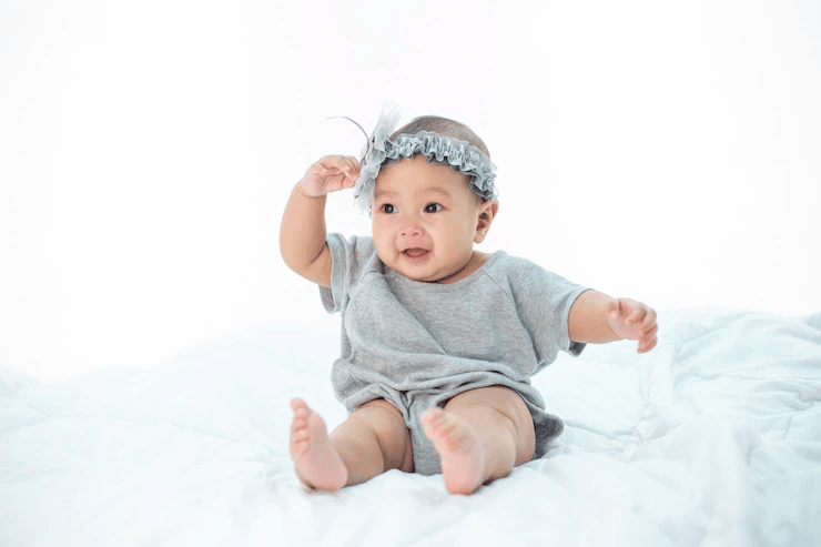 Infant smiling and sitting on a white bed