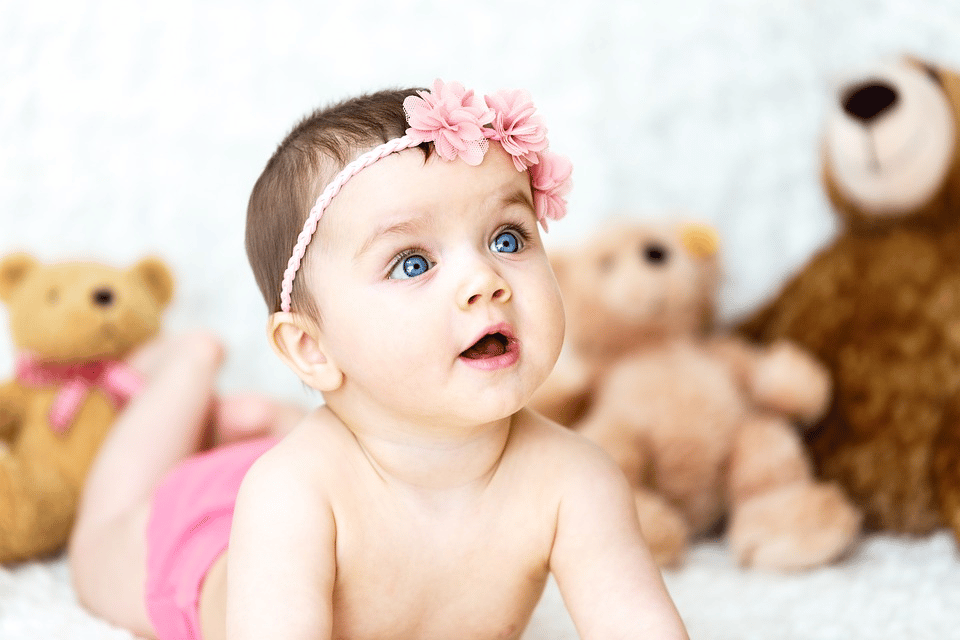 A baby with a flower headband surrounded by teddy bears