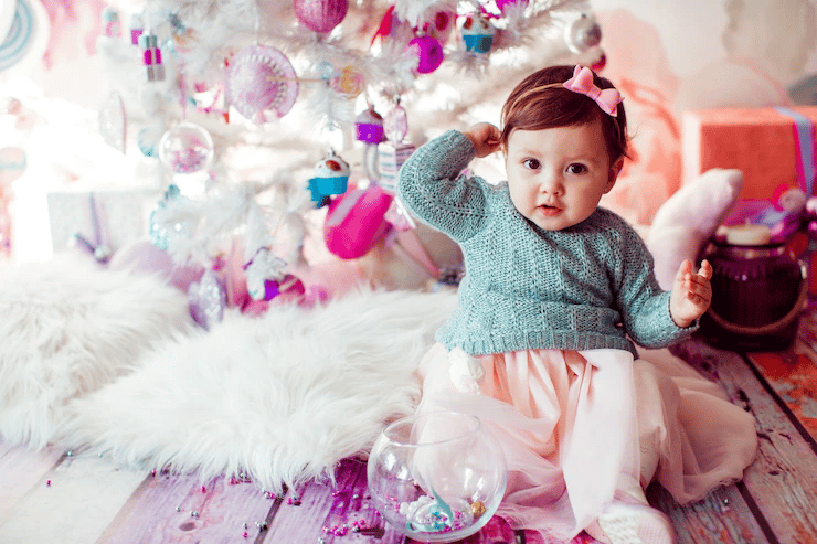 Lovely baby on a plush carpet in front of Christmas tree.