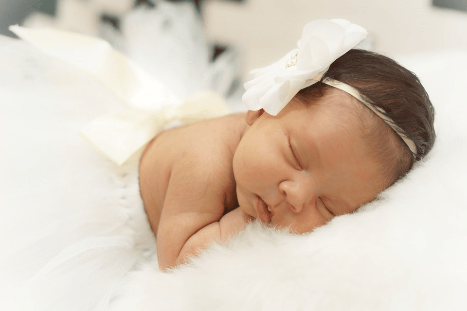 A cute baby dressed in white sleeping in all fours